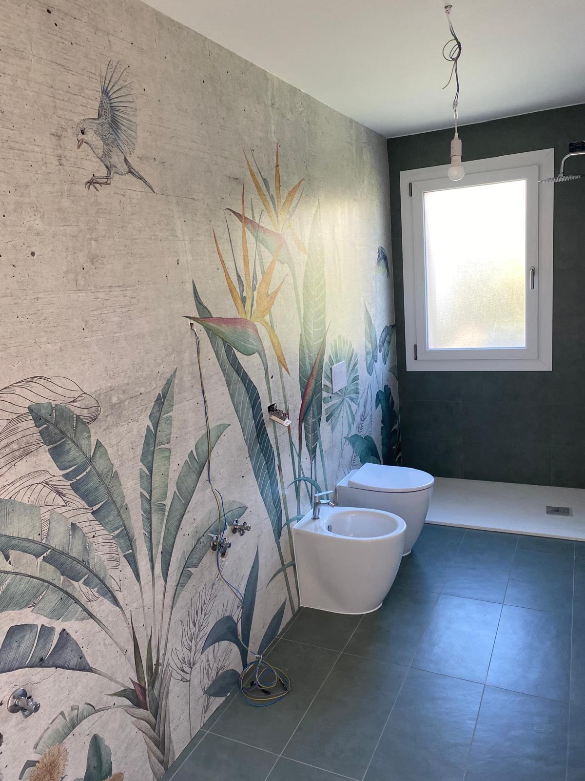 Bagno con carta da parati botanica, rivestimento verde e sanitari bianchi.
