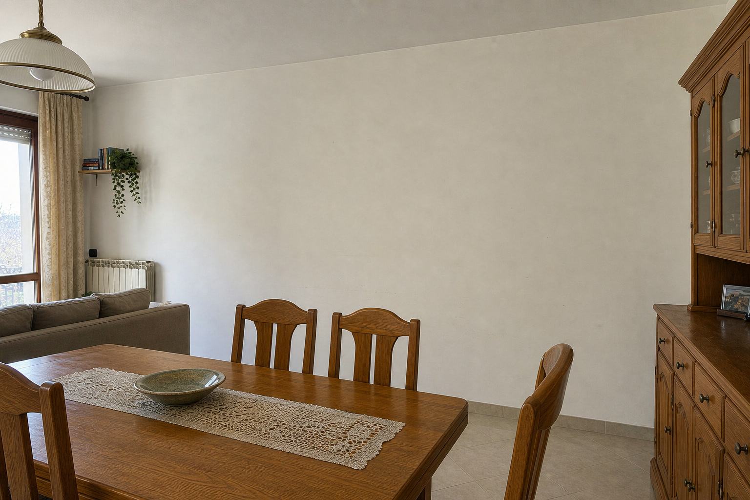 Simulazione prima della ristrutturazione: zona pranzo con parete neutra, tavolo e credenza in legno in stile anni Novanta.