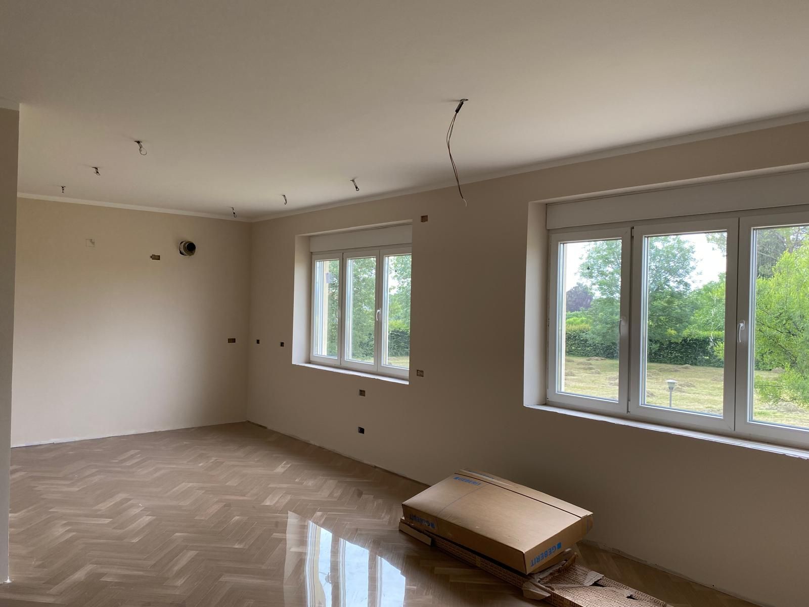 Ambiente interno con pareti chiare, pavimento in legno e finestre affacciate sul verde.